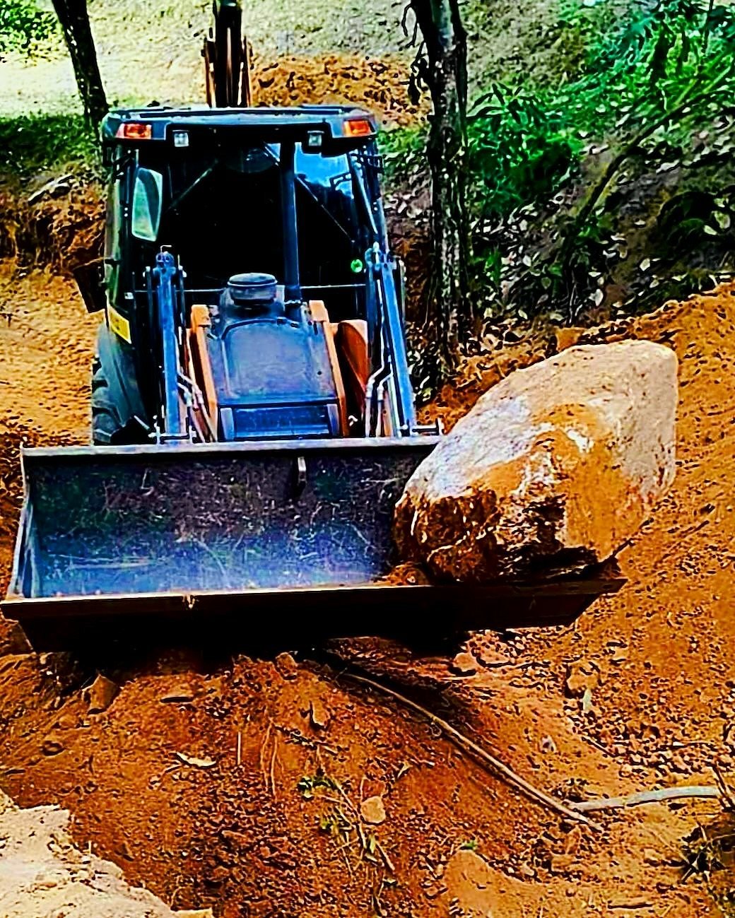 Retroescavadeira removendo pedra grande com a concha frontal em terreno em Timóteo