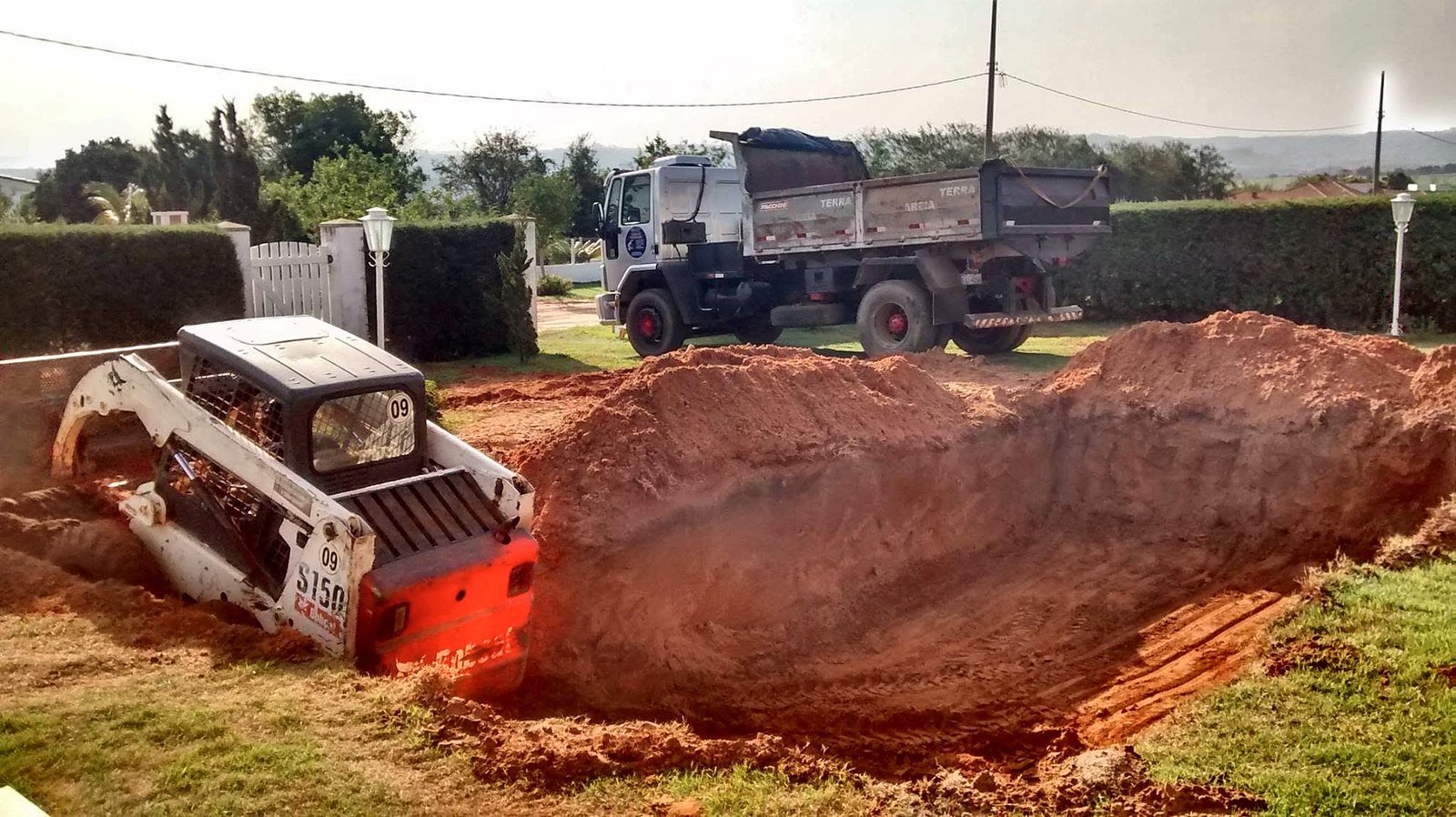 Escavação de piscina com minicarregadeira em chácara de Boituva, com terra vermelha retirada e caminhão basculante