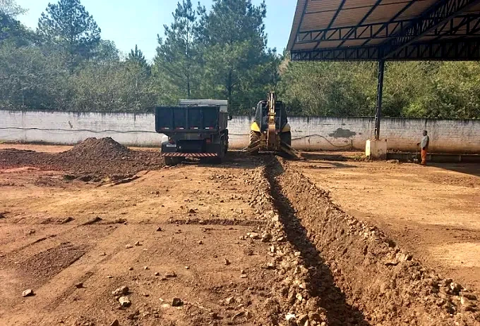Caminhão caçamba e retroescavadeira em serviço de nivelamento e valeta em Canoas/RS