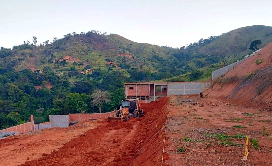 Lote em encosta com talude de terra vermelha e retroescavadeira fazendo terraplanagem em Timóteo MG