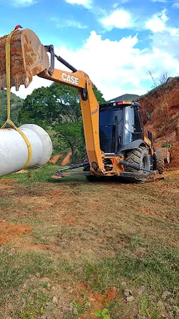 Retroescavadeira içando tubo de concreto para vala de drenagem em Timóteo