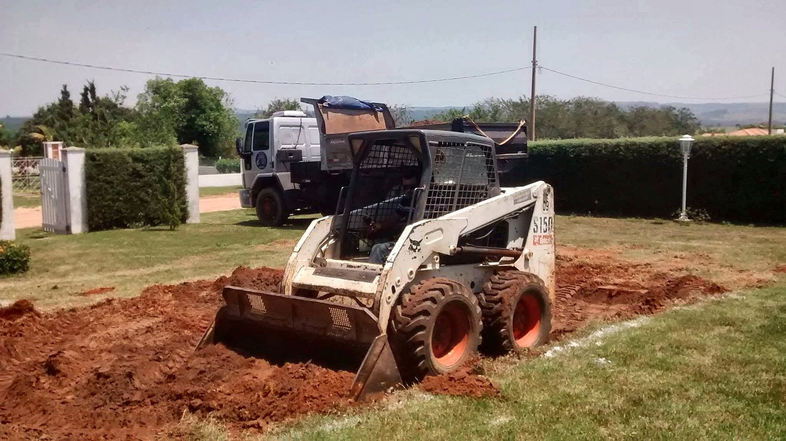 Minicarregadeira Bobcat S150 da WJC Serviços fazendo terraplanagem em chácara de Boituva, com caminhão basculante ao fundo