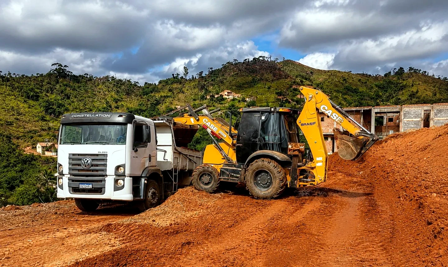 Retroescavadeira Case carregando caminhão basculante com terra vermelha em obra de terraplanagem em Timóteo MG